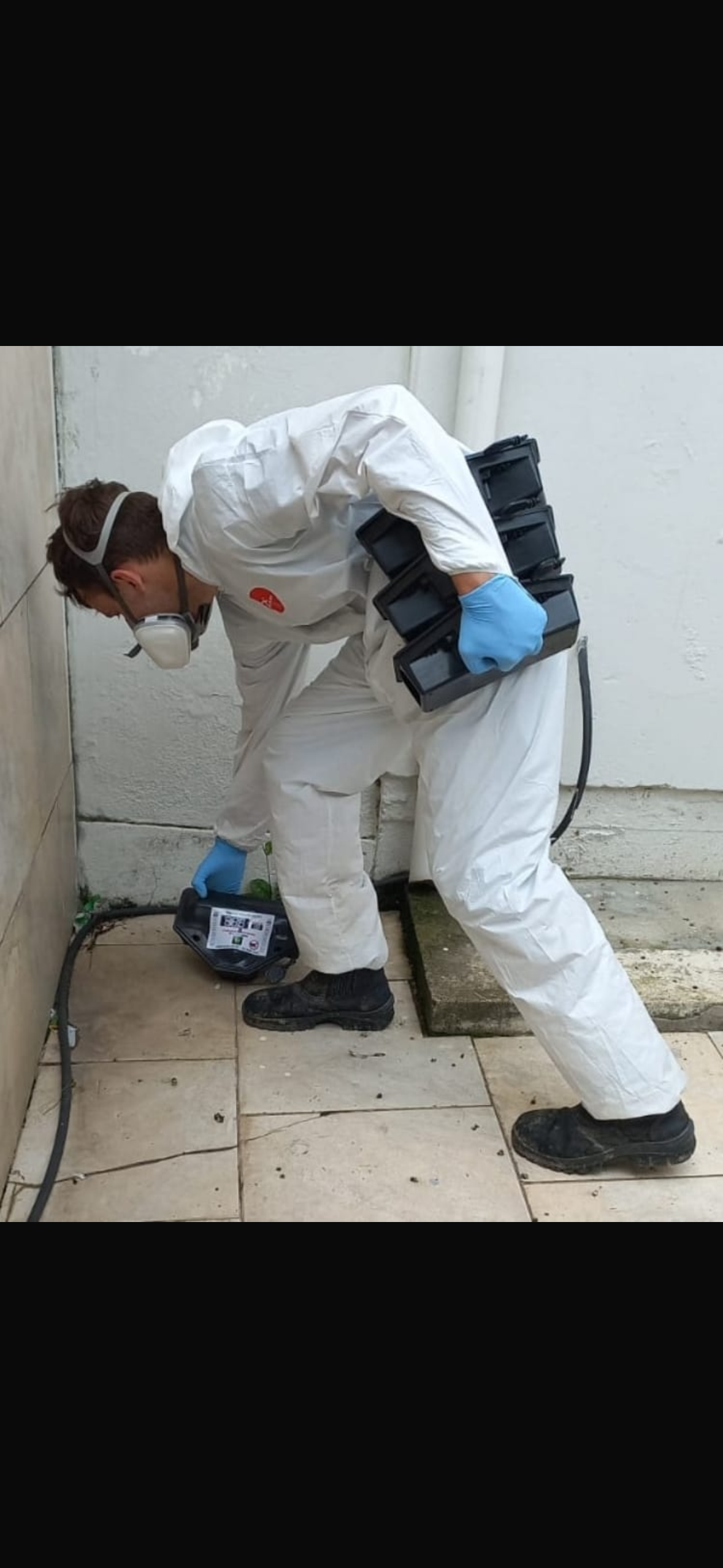 Técnico NOVAECO com macacão branco e pulverizador aplicando produto em rodapé — controle de baratas e insetos